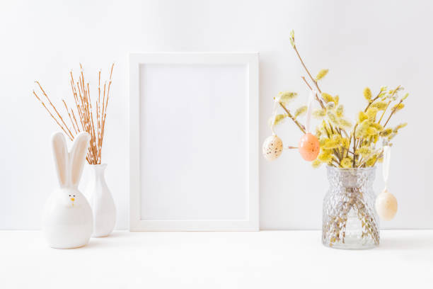 istock Home interior with easter decor. Mockup with a white frame and willow branches in a vase on a light background 1300195448