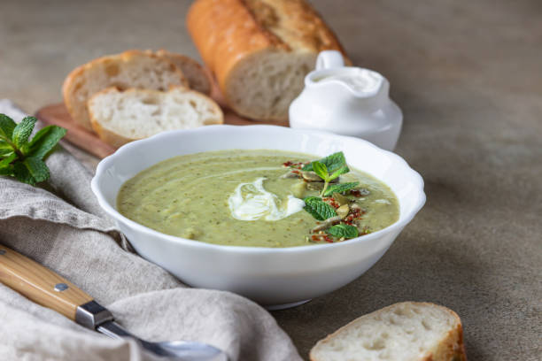 zupa z brokułów podawana z miętą, śmietaną, nasionami i świeżym chlebem na betonowym tle. zdrowa koncepcja wegetariańska. - soup zucchini spinach cream zdjęcia i obrazy z banku zdjęć