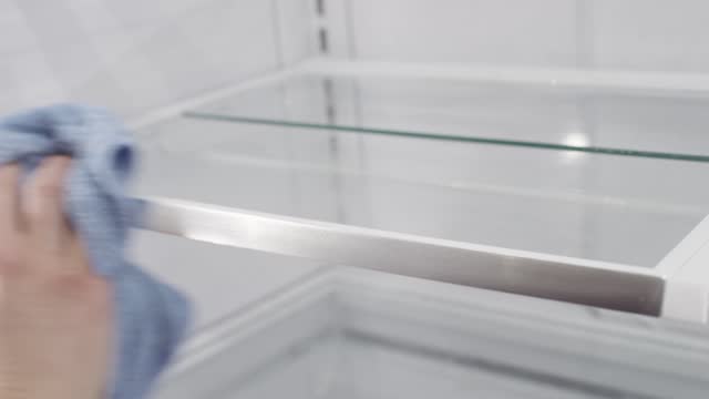 A hand with rag cleans empty shelves inside a refrigerator