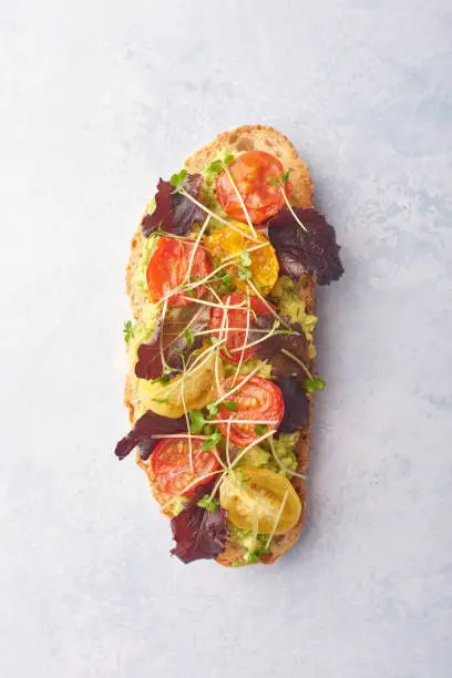 Avocado on toast with cherry tomatoes and cress on a pale backgound