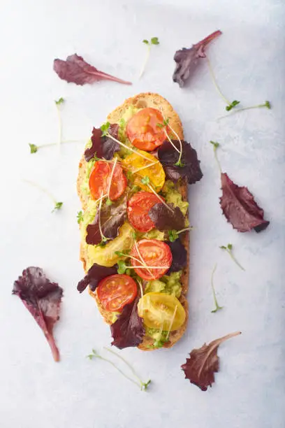 Avocado on toast with cherry tomatoes and salad on a pale background with salad leaves scattered on background