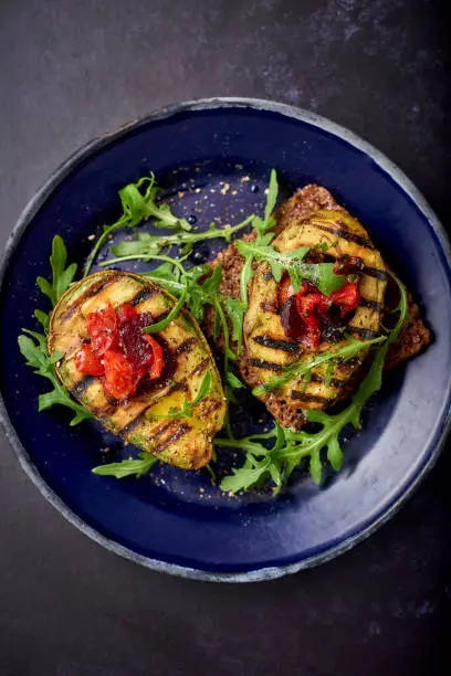 Baked avocado with a tomato salsa and rocket leaves on a dark blue enamel plate