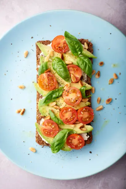 Sliced avocado on rye bread with cherry tomatoes, basil and pine nuts