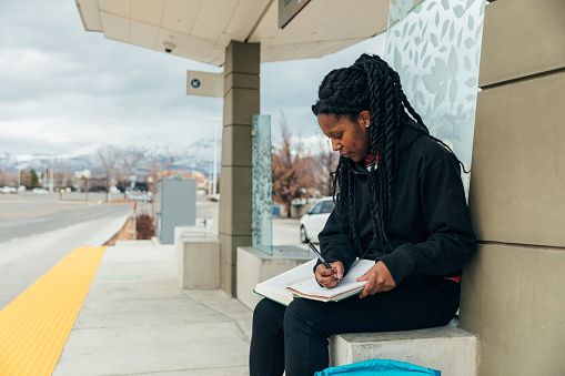A female college student is at a bus stop waiting for the next bus. She is using public transportation to get to university or college campus and class. Image taken in Utah, USA.