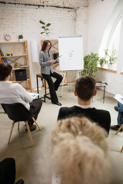 istock Female speaker giving presentation in hall at workshop. Audience or conference hall. Rear rview of unrecognized participants. 1300209424