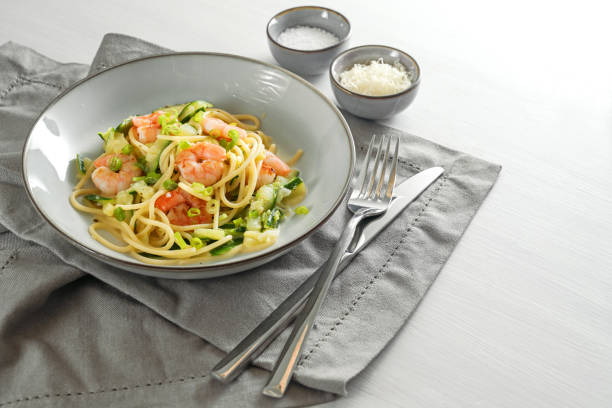 istock Spaghetti with zucchini courgettes, spring onions and prawns in a grey plate on a white table with a napkin and cutlery, healthy cooking concept, copy space 1300212164