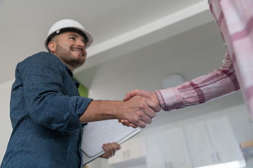 Close-up on a Latin American architect closing a deal with a handshake with a customer about a remodeling project at home