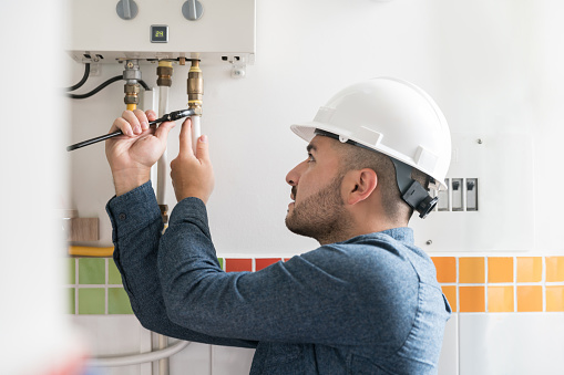 Portrait of a Latin American Repairman installing a natural gas boiler at a house using a wrench - home improvement concepts
