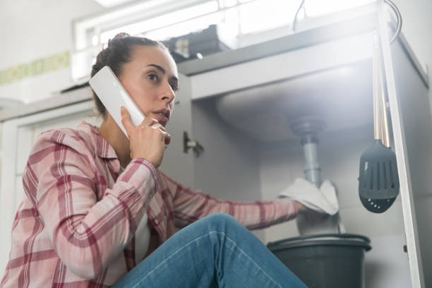 mujer en casa llamando a un fontanero sobre una tubería con fugas en su fregadero - sink drain plumber domestic kitchen fotografías e imágenes de stock