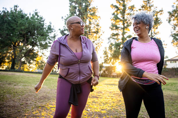 due donne di colore che camminano attraverso un campo di erba - senior adult senior couple exercising african ethnicity foto e immagini stock
