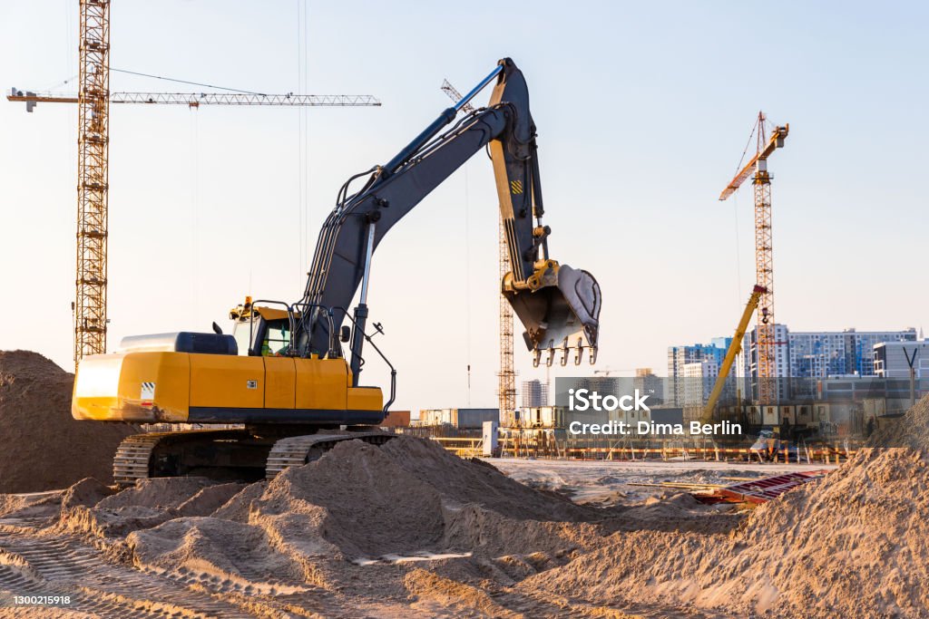 Group tower cranes and excavator silhouette at construction site, sunset sky background Group tower cranes and excavator silhouette at construction site, sunset sky background.Future residential high-rise complex Backhoe Stock Photo