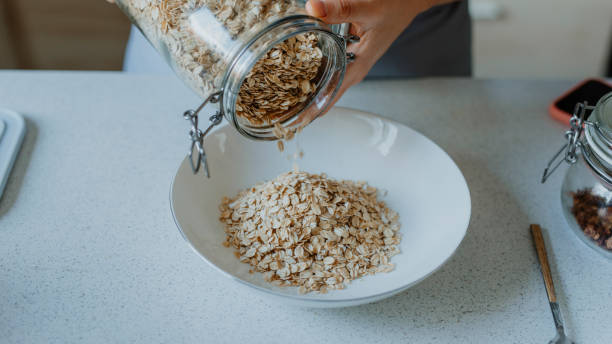 fare una colazione sana e nutriente: mani di una donna che versa avena arrotolata in una ciotola - oat oatmeal rolled oats oat flake foto e immagini stock