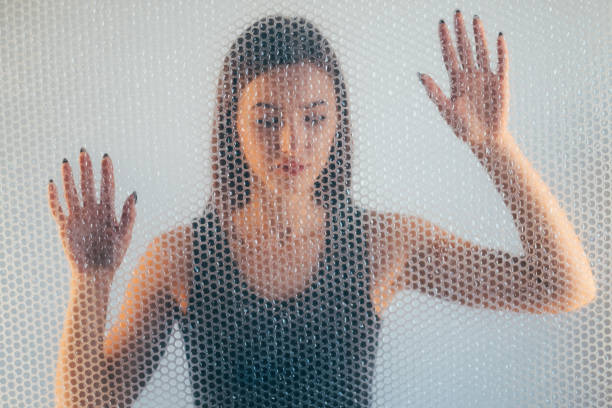 Woman protection. Defocused portrait. Self isolation. Female discrimination. Hopeless lady in black top trapped behind transparent bubble pack texture wall on light background out of focus.