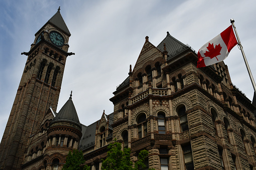 Tower and part of the facade of Old City Hall in Toronto, seen from below, with a Canadian flag.