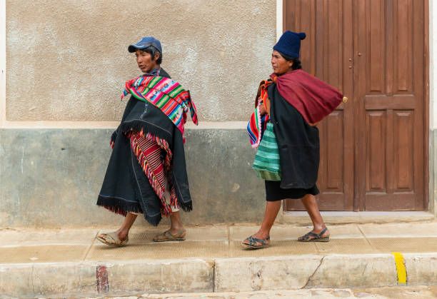 Two Bolivian Tarabuco indigenous in traditional clothing walking in a street with colonial architecture near Sucre city.
