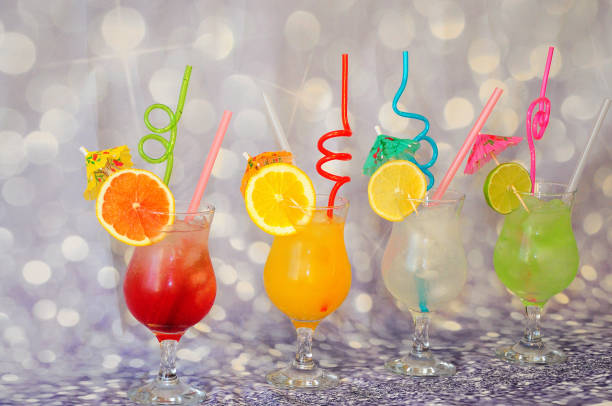 Four glasses with different citrus juices with ice and slices of grapefruit, lemon, lime and orange on a gray shiny background.