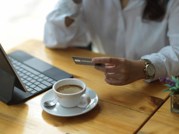 istock Female hand holding credit card while sitting at workplace with digital tablet and coffee cup 1300237817
