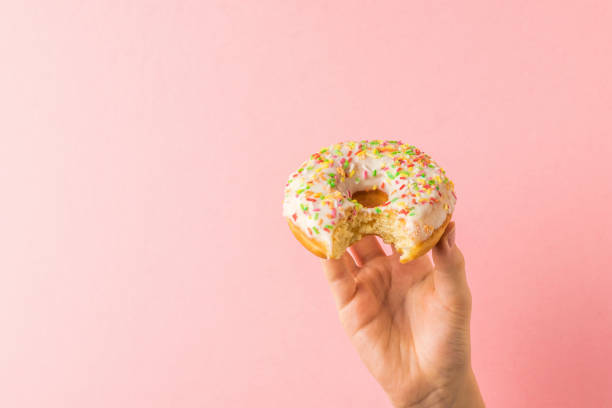 istock A child's hand with a nibbled donut on a light pink background. 1300240443