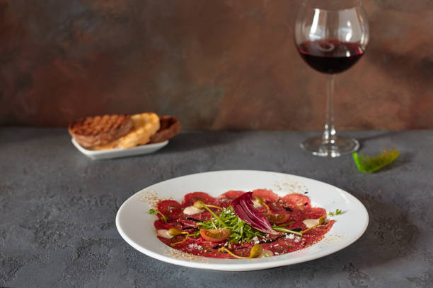 carpaccio de viande dans une plaque blanche sur un fond en bois, avec le pain et le vin délicieux dans un verre - carpaccio red meat caper bread photos et images de collection