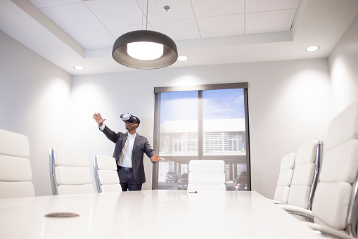 An African American Male office worker using a virtual reality headset to work.