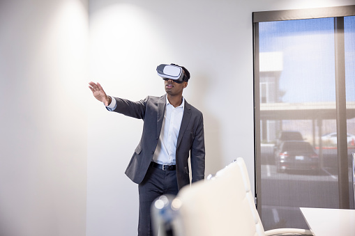 An African American Male office worker using a virtual reality headset to work.