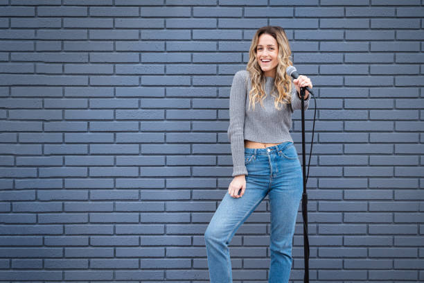 Young Blonde Female Comedian Against Blue Grey Brick Wall with Microphone and Expressions Young Comedian against grey gray brick wall with microphone and stand making an expression comedian stock pictures, royalty-free photos & images