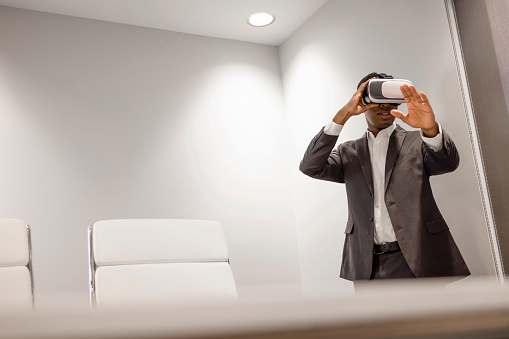 An African American Male office worker using a virtual reality headset to work.