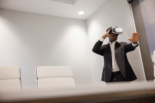 An African American Male office worker using a virtual reality headset to work.