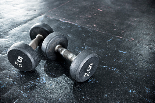 A pair of dumbbells of moderate weight lying on worn black rubber floor panels at a gym or fitness center.