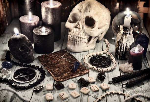 istock Scary skull with runes, black candles and magic objects on witch table. 1300260659