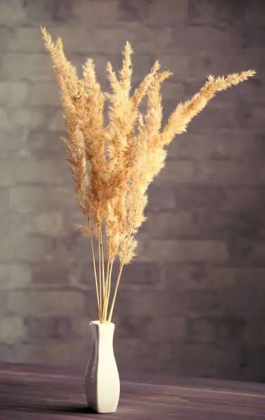 Photo of Vertical image of dry field spikelets, young reed grass in a white vase on the wooden surface of the table