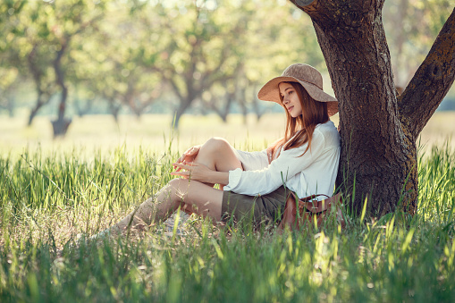 young girl in a straw hat travels green meadows. Beautiful red-haired hipster woman in a green garden