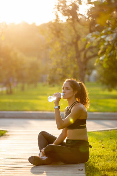 istock Young woman sitting on a break from jogging and drinking bottled water 1300266290