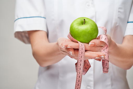 nutritionist doctor healthy lifestyle concept - holding organic fresh green apple and measure tape.