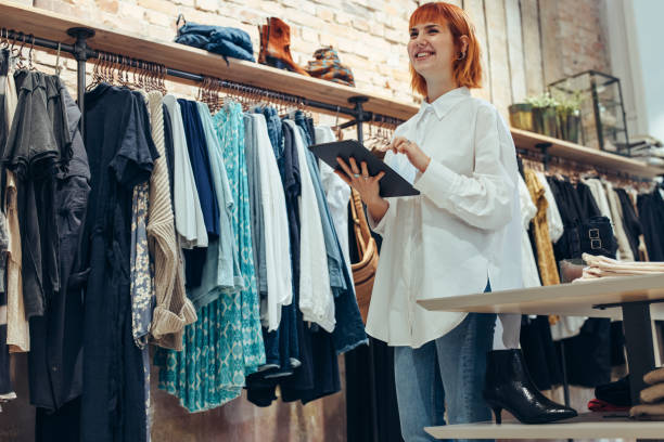 Shop owner with a digital tablet Young shop owner with a digital tablet. Woman working in clothing store with a table pc in hand looking away and smiling. clothing store stock pictures, royalty-free photos & images