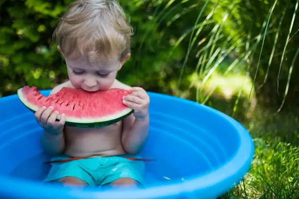 Photo of Cute little toddler boy taking a bath in garden and eat watermelon