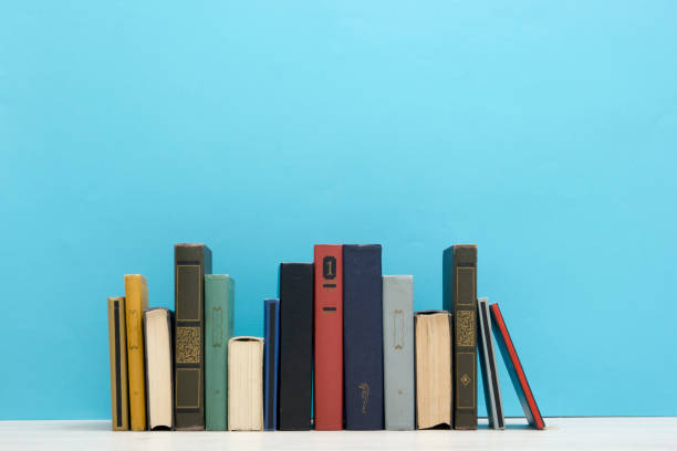 istock Books on bookshelf in Library. Back to School education concept on colored abstract blue background. Open hardback book stack in a raw on wooden desk table. 1300277790