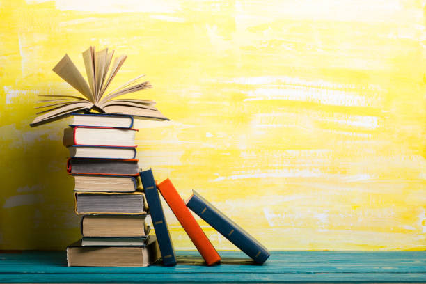 istock Books on bookshelf in Library. Back to School education concept on colored abstract yellow background. Open hardback book stack in a raw on wooden desk table. 1300277813