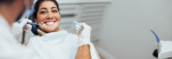 Dentist examining teeth of a female patient in dental clinic using dental tools. Happy woman getting dental treatment.