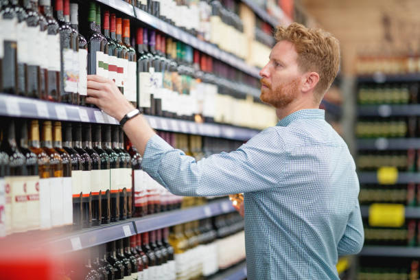 Man picking up wine in supermarket Young man with beard picking up wine in supermarket alcohol shop stock pictures, royalty-free photos & images