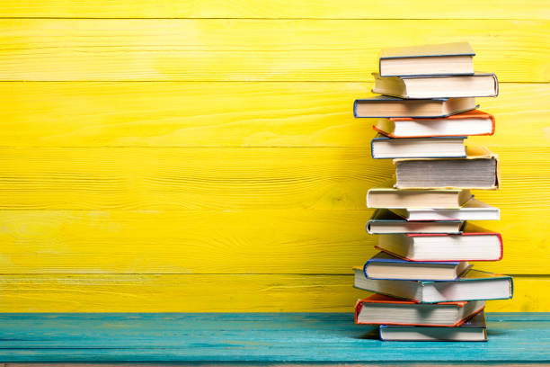 istock Books on bookshelf in Library. Back to School education concept on colored abstract yellow background. Open hardback book stack in a raw on wooden desk table. 1300279599