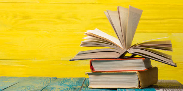istock Books on bookshelf in Library. Back to School education concept on colored abstract yellow background. Open hardback book stack in a raw on wooden desk table. 1300280183