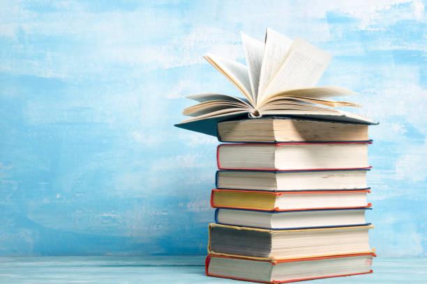 istock Books on bookshelf in Library. Back to School education concept on colored abstract blue background. Open hardback book stack in a raw on wooden desk table. 1300280232