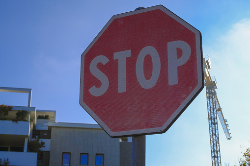 stop sign close-up against buildings, building crane, blue sky. Transportation, road signs