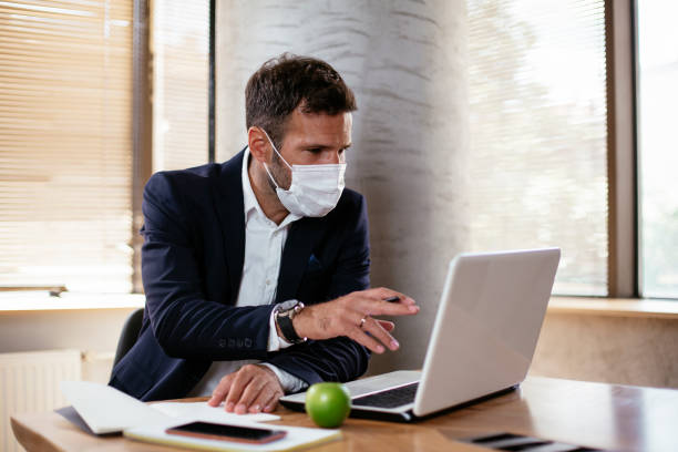 istock Young businessman with a mask working in his office on laptop. 1300285739