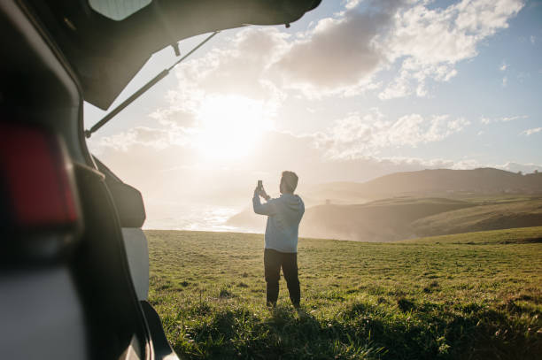 istock Young man taking a picture with a smart phone by his car 1300287196