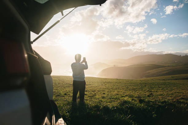 istock Young man taking a picture with a smart phone by his car 1300287200