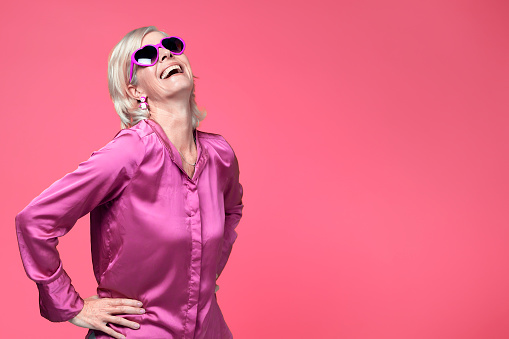 Portrait of a creative, colorful senior woman against a pink background.