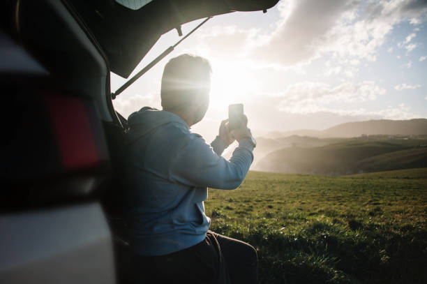 istock Young man taking a picture with a smart phone by his car 1300287286