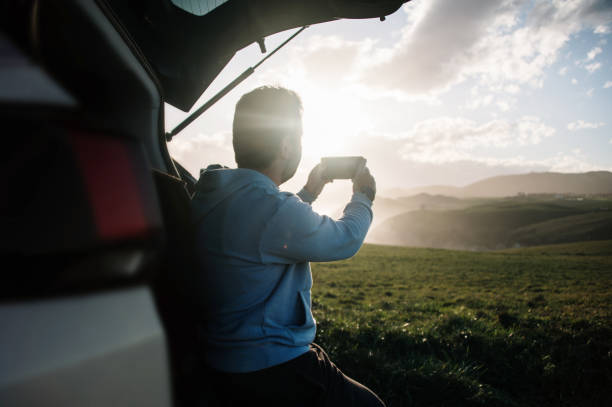 istock Young man taking a picture with a smart phone by his car 1300287313
